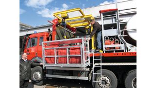 Zeigt einen Feuerwehr-LKW mit montiertem Halbportalkran der Feuerschutz Messer AG zum Be- und Entladen des LKWs mit Ladeplattformen mit Schlauch-Transportgestellen, Schlauchbrücken und Ausgleichsbehältern samt Zubehör. (Bild: Nozag)
