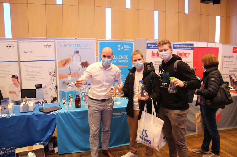 Tatsächlich gibt es neben Fachwissen auch einiges Handfestes zum mitnehmen auf der Messe. Nicht etwa die Glaskolben, die DWK-Mitarbeiter Eric Lehnen (ganz links) hier den Besuchern fürs Foto in die Hand gegeben hat. Aber z. B. die neongrüne Silikonabdeckung, die auf dem Erlenmeyerkolben rechts zu sehen ist.  Weitere Infos zu den kommenden LAB-SUPPLY-Messen finden Sie auf www.lab-supply.info.  (LABORPRAXIS, C. Lüttmann)