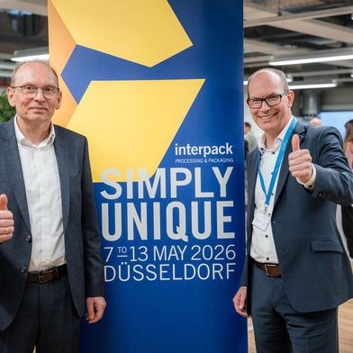 Interpack-Direktor Tomas Dohse (rechts) und Optima-CEO Dr. Stefan König (links) posieren vor dem Motto der Interpack: Simply Unique. (Bild: Messe Düsseldorf)