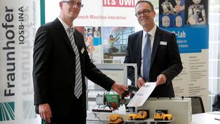 Thomas Eisenbach (RTB GmbH & Co. KG, links) demonstriert Günter Korder (Geschäftsführer it's OWL Clustermangement GmbH) das neue Assistenzsystem für die Montage von Verkehrsgeräten, bei dem der Werker über einen Barcodescanner geführt wird. (it's OWL, Adamski)