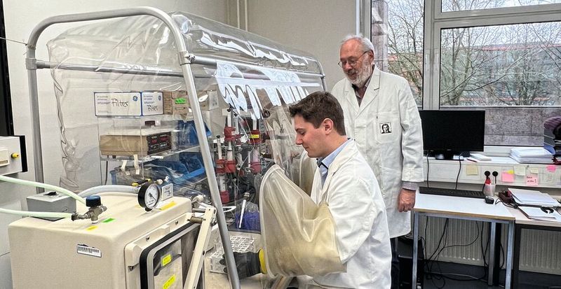 Raphael Trischler (sitzend) und Volker Müller im Labor an einer Anaerobenkammer. Diese enthält keinen Sauerstoff, sondern Stickstoff, sodass Sauerstoff-sensible Bakterien wie Blautia luti darin gefahrlos gehalten werden können.(Bild:  Jennifer Roth, Goethe-Universität Frankfurt)