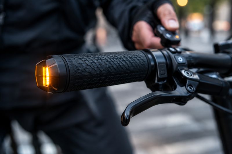 Sicher abbiegen, beide Hände am Lenker: Zugelassene Fahrradblinker (mit K-Nummer oder E-Prüfzeichen) werden bequem per Knopfdruck bedient und dürfen das Handzeichen im Verkehr offiziell ersetzen. (Bild: KI-generiert / Dall-E)