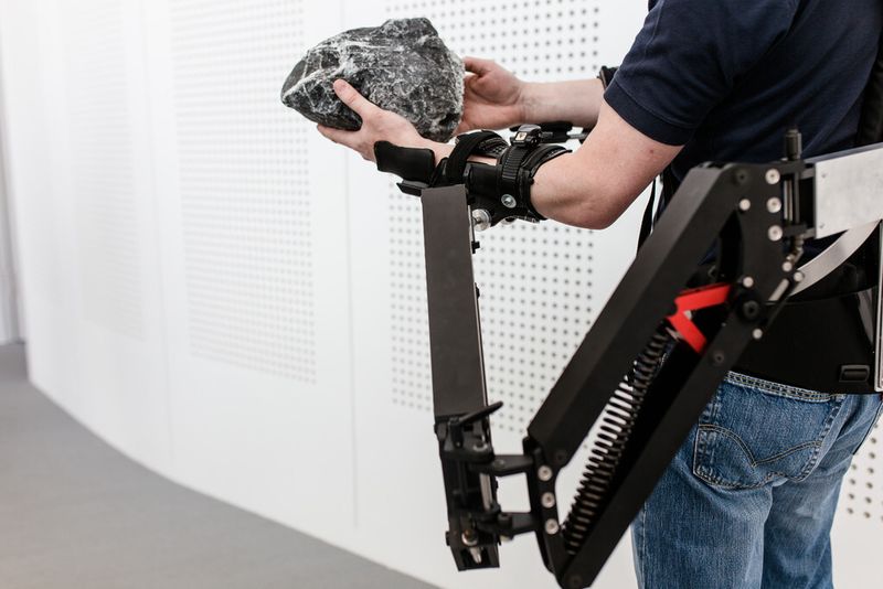 Dr. Konrad Stadler, Dozent für Regelungstechnik, Zürcher Hochschule für Angewandte Wissenschaften, demonstriert die Funktionsweise des Exoskeletts. Zu sehen ist die passive Unterstützung zum Heben schwerer Lasten. (Bild: Ludmilla Parsyak/Fraunhofer IAO)
