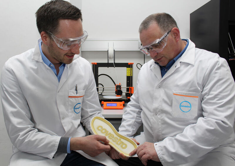 Jörg Tillack (rechts) und Lukas Breuers, beide sind Digitaldruck-Spezialisten bei Covestro, begutachten eine Schuhsohle mit aufgedrucktem Klebstoff. Im Hintergrund ist ein Drucker zu erkennen, der nach dem Schmelzschichtverfahren (FFF) den Klebstoff appliziert hat. (Covestro)