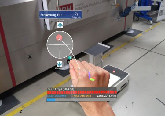 (Blick durch die AR-Brille: Der Screenshot zeigt die Benutzeroberfläche für die Gestensteuerung. Logistikmitarbeiter müssen lediglich den roten Punkt greifen, der als virtueller Joystick dient – schon können sie das Fahrzeug bewegen. Foto: IPH, Florian Kreutzjans)