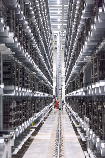 Insgesamt bietet das Produktions-Pufferlager (Logistikmodul) 2.300 Lagerplätze. Zwischen den beiden Regalen verrichten zwei Regalbediengeräte vollautomatisiert ihre Arbeit. Sie bevorraten die aus der Fertigung angelieferten Härtegestelle mit den Produkten und geben diese an die Ofenanlage aus. (Bild: Leuze)