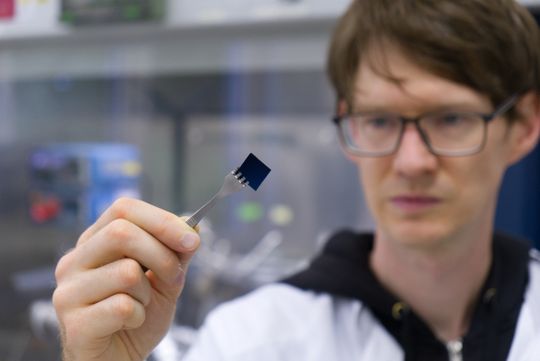 Stefan Schröder hält eine mit einer hauchdünnen Polymerbeschichtung versehene Siliziumprobe. Die Beschichtung ist mit bloßem Auge nicht sichtbar.(Bild:  Uni Kiel/C. Anders)