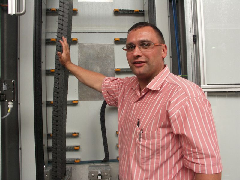 Enrico Sperling zeigt, dass in der vertikalen Kantenschleifmaschine für die Energiezuführung verschiedene Energieführungs-Systeme zum Einsatz kommen. (Bild: Igus)