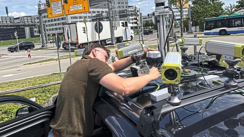 TUM-Forscher Erik Leo Haß prüft die Sensorik auf dem Fahrzeug an einer Kreuzung in Garching-Hochbrück. Aus den unterschiedlichen Echtzeit-Messungen von Kameras, Lidaren und Radaren wird ein permanent aktualisiertes Bild der Verkehrssituation erstellt.(Bild:  A.Schmitz / TUM)