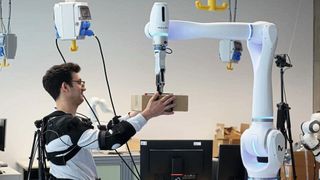 Researcher Federico Masiero receives a package whose weight the robot has already transmitted to the exoskeleton. (Image: Andreas Schmitz / TUM)