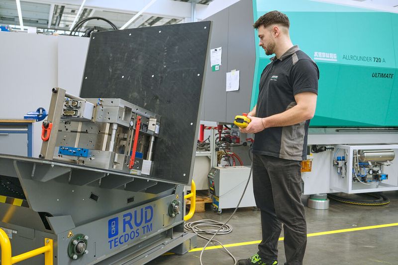 Ein Arburg-Mitarbeiter handhabt ein tonnenschweres Spritzgießwerkzeug auf dem RUD Tecdos TM ergonomisch und sicher. (Bild: RUD / Jensen)