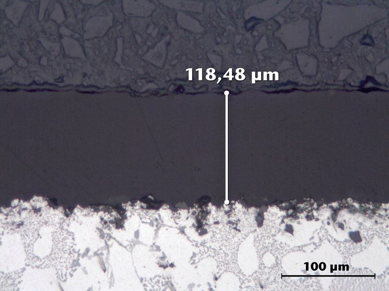 Bild 3: Eine PFA-Doppelschicht schützt Aluminiumguss (hell) vor Korrosion. Aufgrund der molekularen Vermischung ist eine Trennlinie der Einzelschichten nicht zu erkennen (Schliffbild). (Bild: AHC)