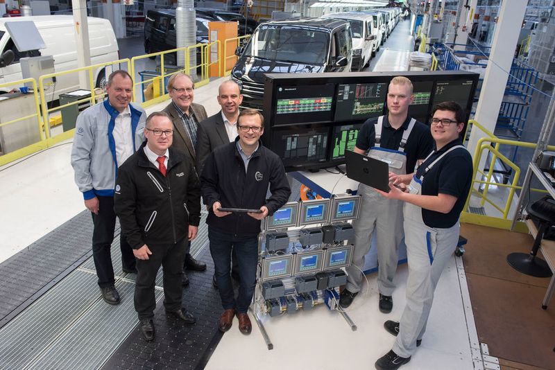 Volker Loebe (Projektleiter Digitalisierung in der Berufsausbildung für die deutschen Volkswagen Werke), Jürgen Jaskolla (Leiter für Fertigungsautomation), Walter Deterding (Betriebsrat Volkswagen Nutzfahrzeuge), Olaf Böker ( Leiter der Volkswagen Akademie Hannover), Rando Ballmann (Projektleiter) und Jannes Ditloff (23, li.) sowie Dennis Schwertfeger (21), beide Auszubildende Elektroniker für Automatisierungstechnik (3. Ausbildungsjahr), an der selbstgebauten Schalt-Tafel mit Komponenten für die Zentrale Anlagenüberwachung. (Bild: Volkswagen Nutzfahrzeuge)