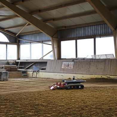 Der autonome Reiterhofassistent glättet aktuell im Dauertestbetrieb den Boden einer Reithalle. 
 (Bild: Fraunhofer IPA)